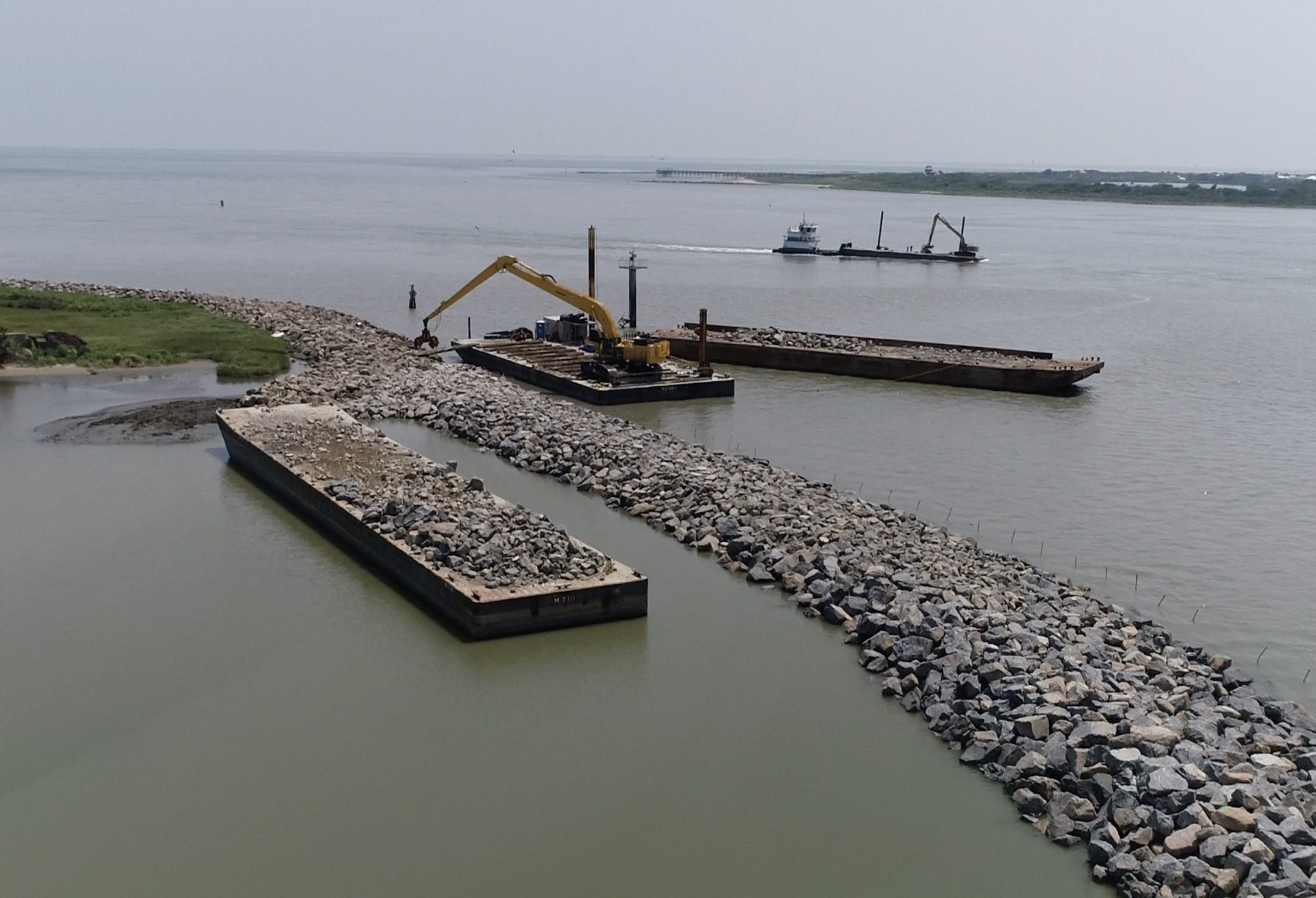 Excavator loading armor stone onto a barge