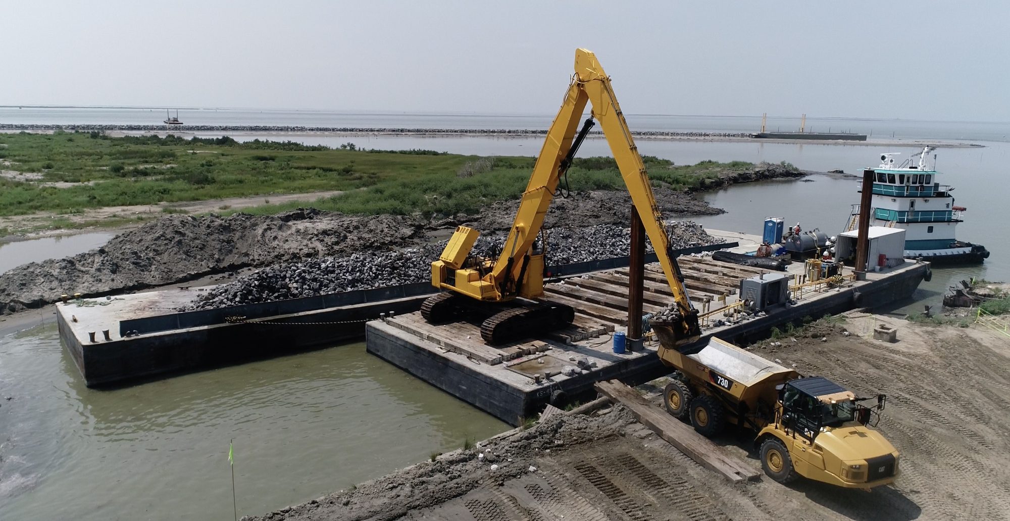 Excavator loading a deck barge from a work boat